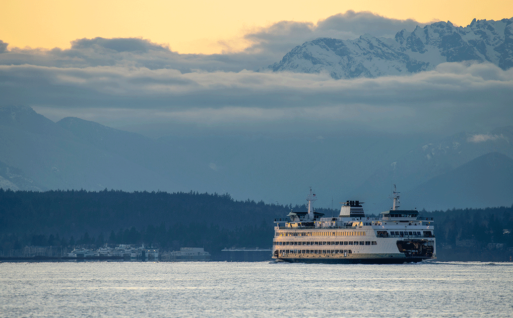 Image of a ferry boat on a waterway with snow-capped mountains in the background.